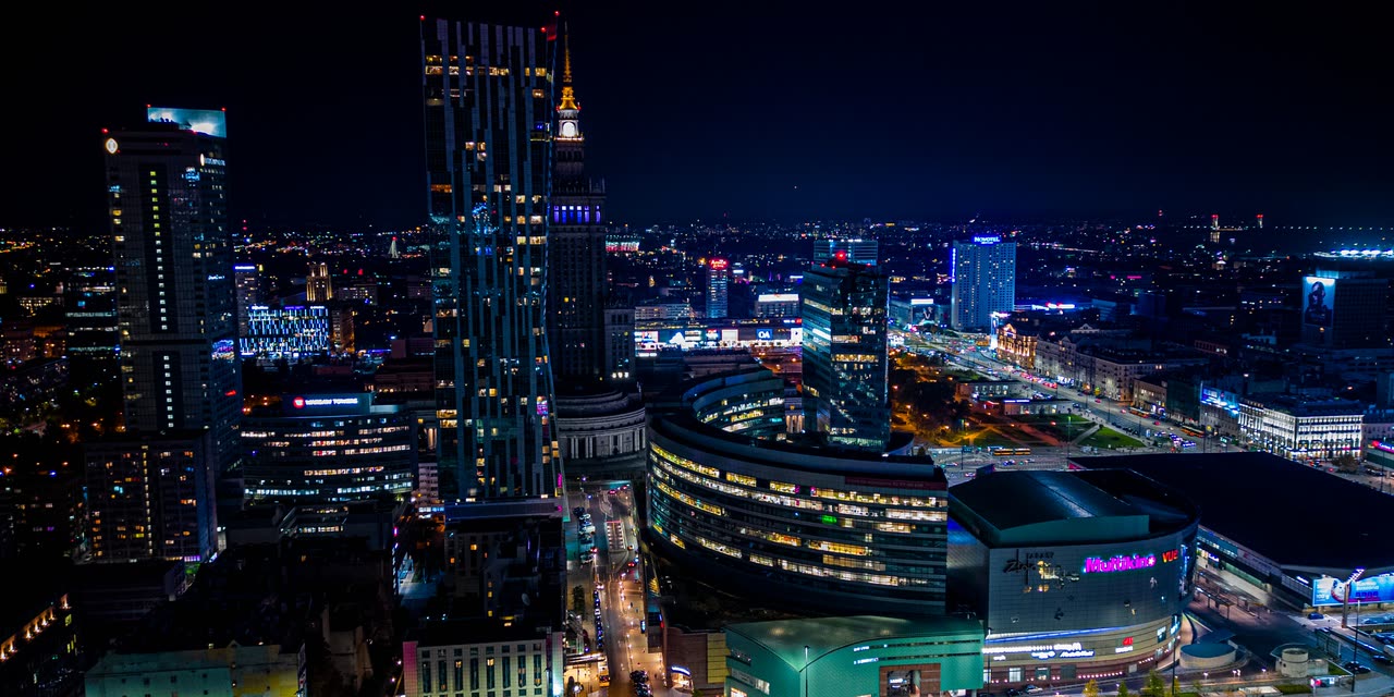 Panorama Warszawy nocą z lotu ptaka — oświetlone wieżowce centrum i siatka ulic