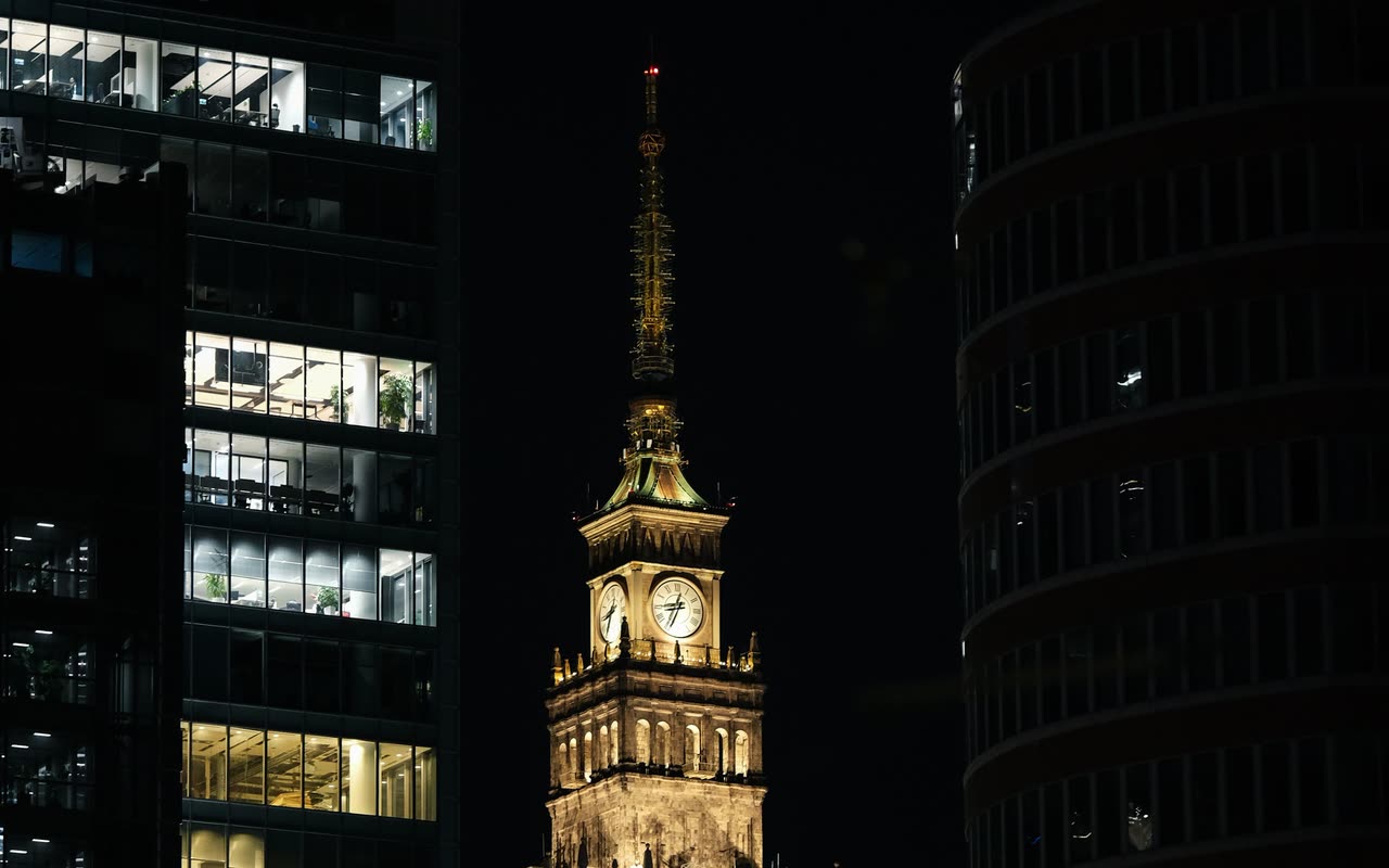 Wieża Pałacu Kultury nocą w ramie ciemnych, masywnych budynków