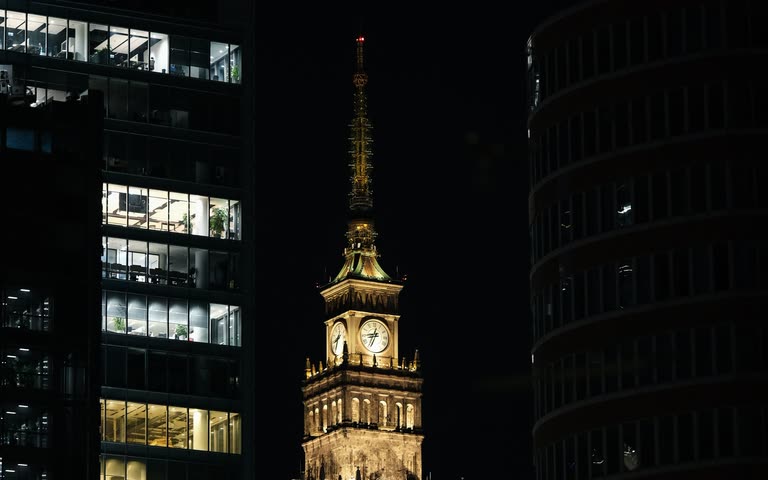Wieża Pałacu Kultury nocą w ramie ciemnych, masywnych budynków
